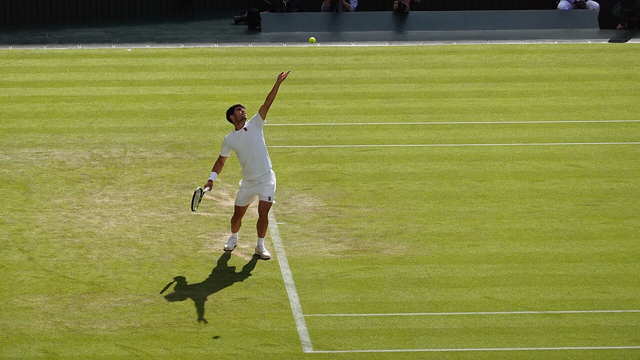 Tennisser strekt zich uit voor de opslag op het gras van Wimbledon
